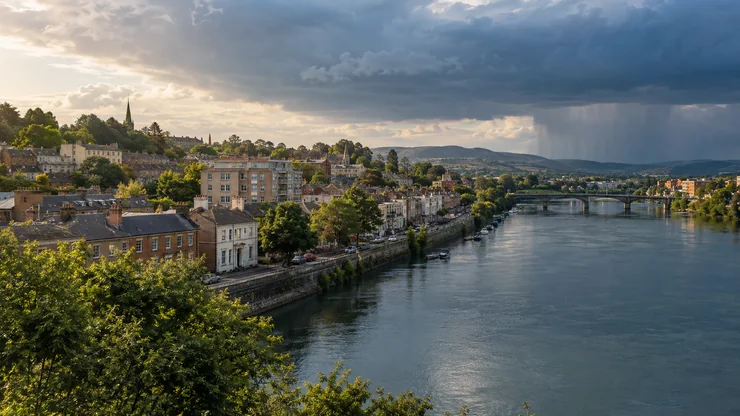 A waterside urban neighbourhood beneath sunlit clouds and an approaching rain front.